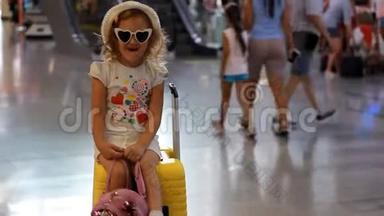 小女孩游客坐在火车站的一个大黄色手提箱上。 儿童正在等待出发，<strong>前往</strong>